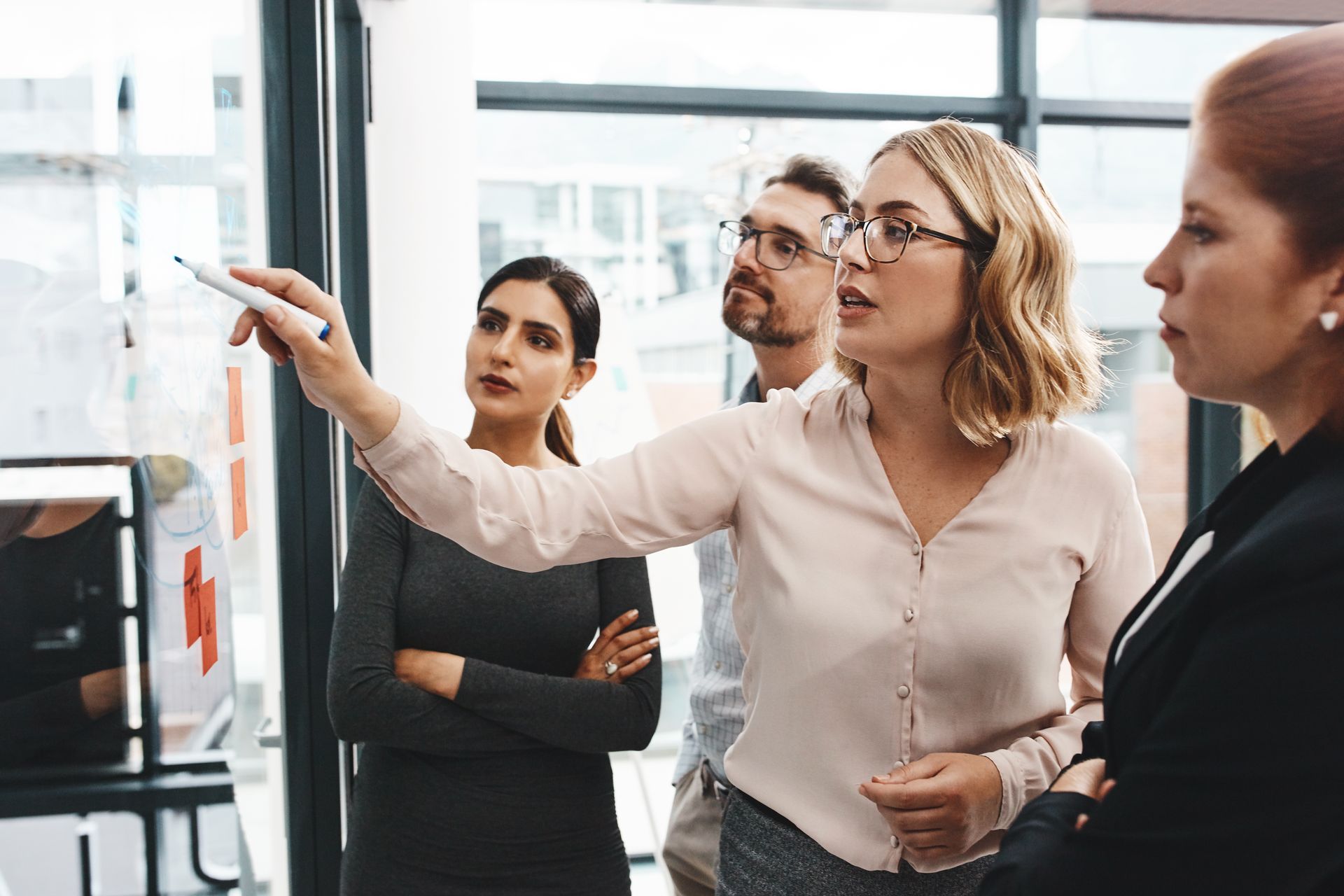 A group of people are standing around a woman using a whiteboard.