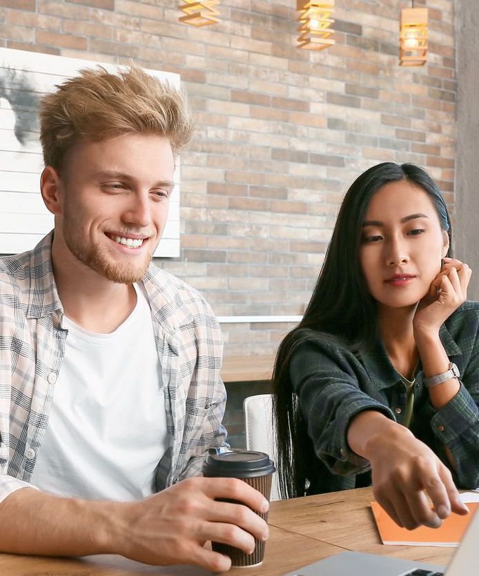 A man and a woman are sitting at a table looking at a laptop computer.