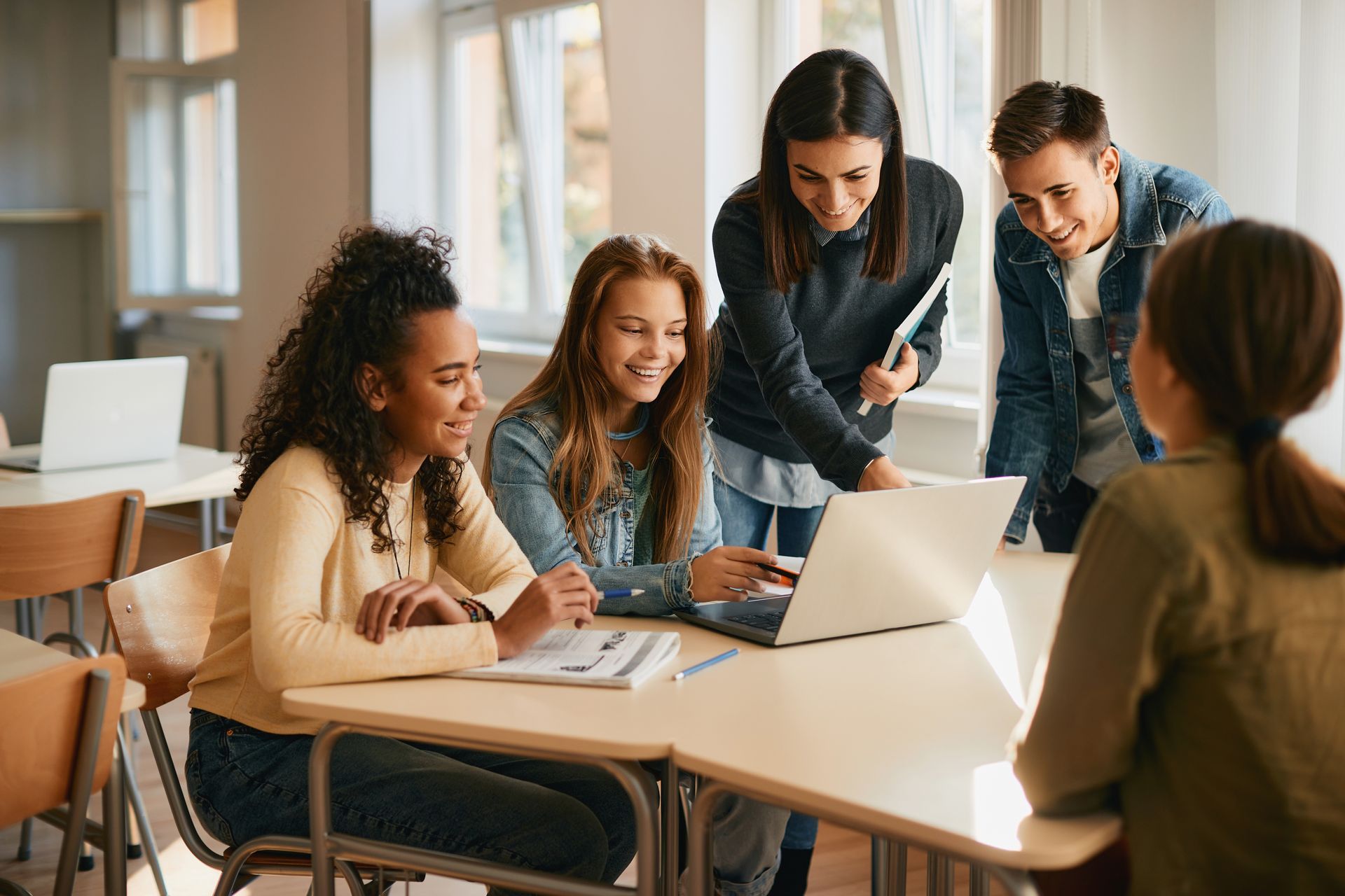 A group of young people are sitting at a table looking at a laptop computer.