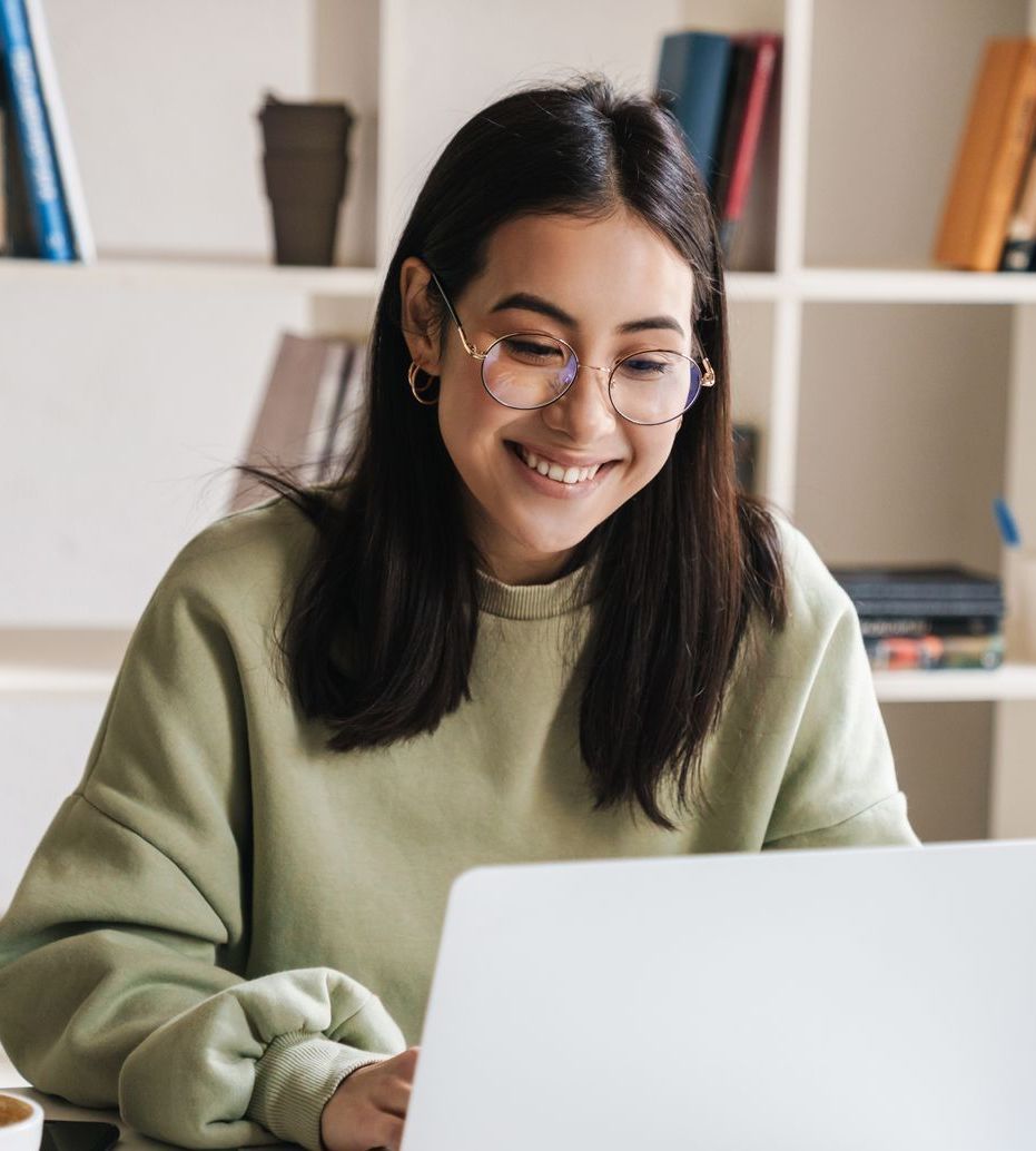 A woman wearing glasses is smiling while using a laptop computer.