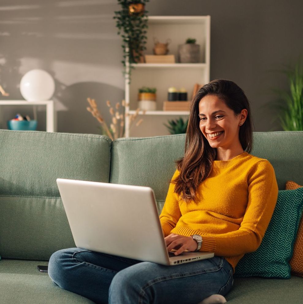 A woman is sitting on a couch using a laptop computer.