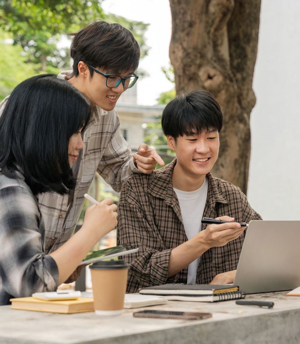 A group of people are sitting around a table looking at a laptop.