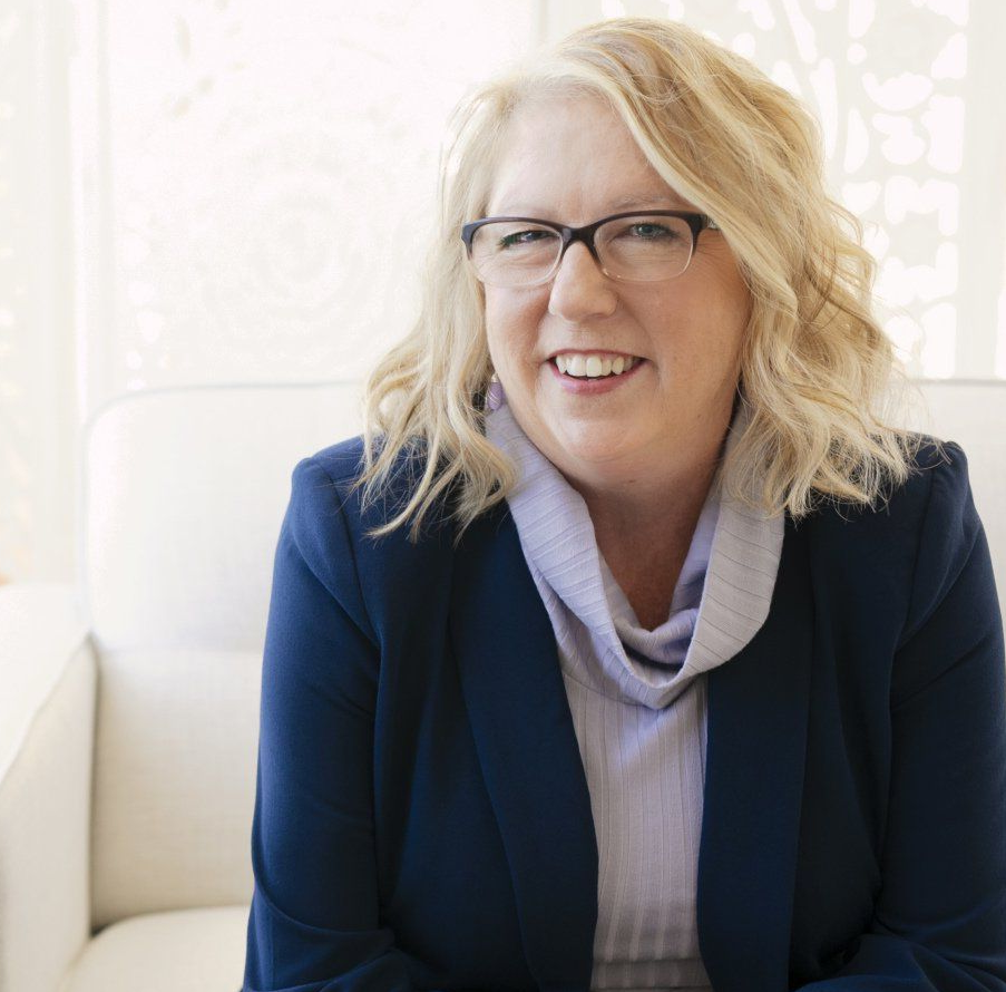 A woman wearing glasses and a blue jacket smiles for the camera