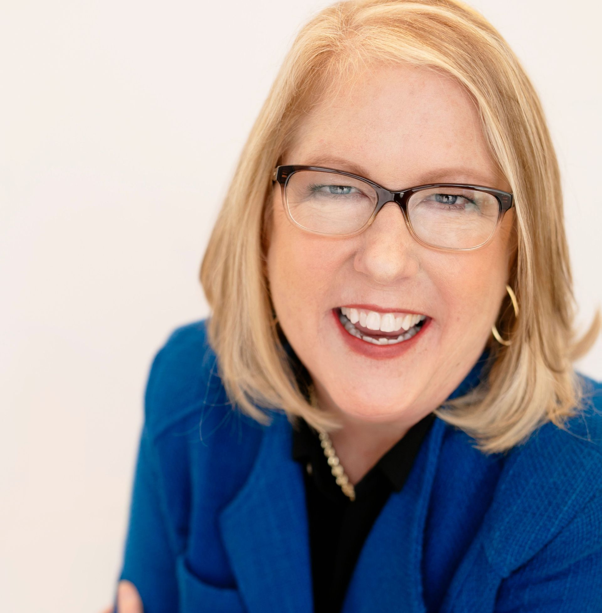 A woman wearing glasses and a blue jacket smiles for the camera