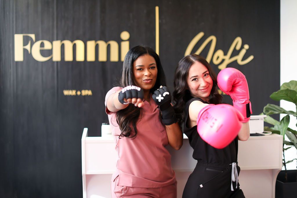 Two women wearing pink boxing gloves are standing next to each other in front of a sign that says femmi
