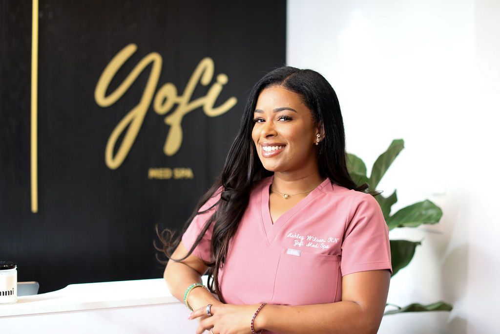 A woman in a pink scrub top is standing in front of a sign.
