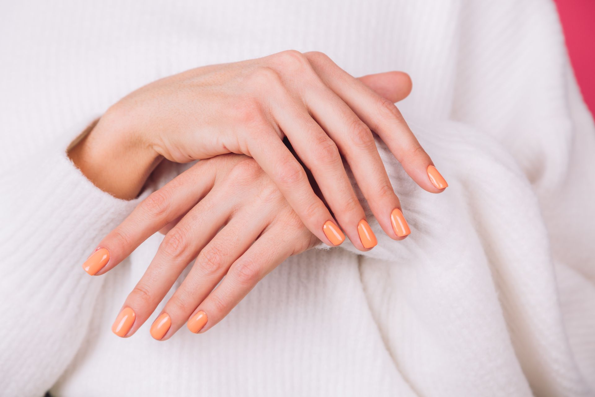 Hands with peach-colored nail polish crossed over a white sweater.