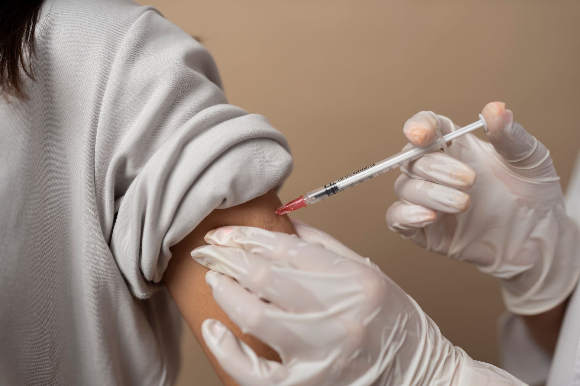 Person receiving an injection in their upper arm; syringe held by gloved hand.