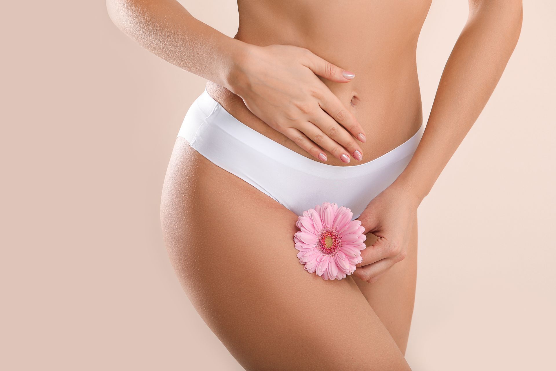 Woman in white underwear holding pink flower near abdomen.