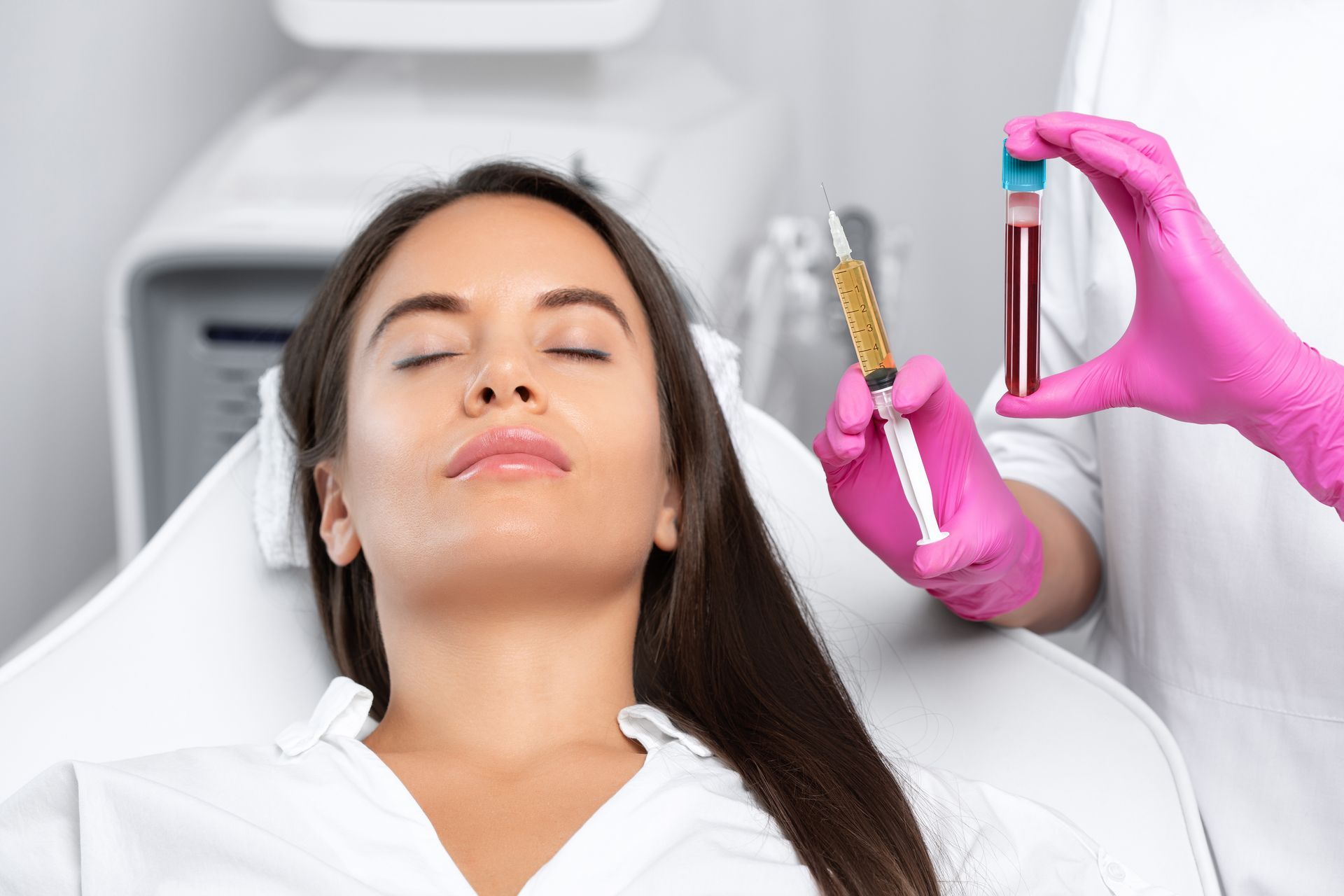 A woman is getting a facial treatment in a hospital while a doctor holds a syringe and a test tube.