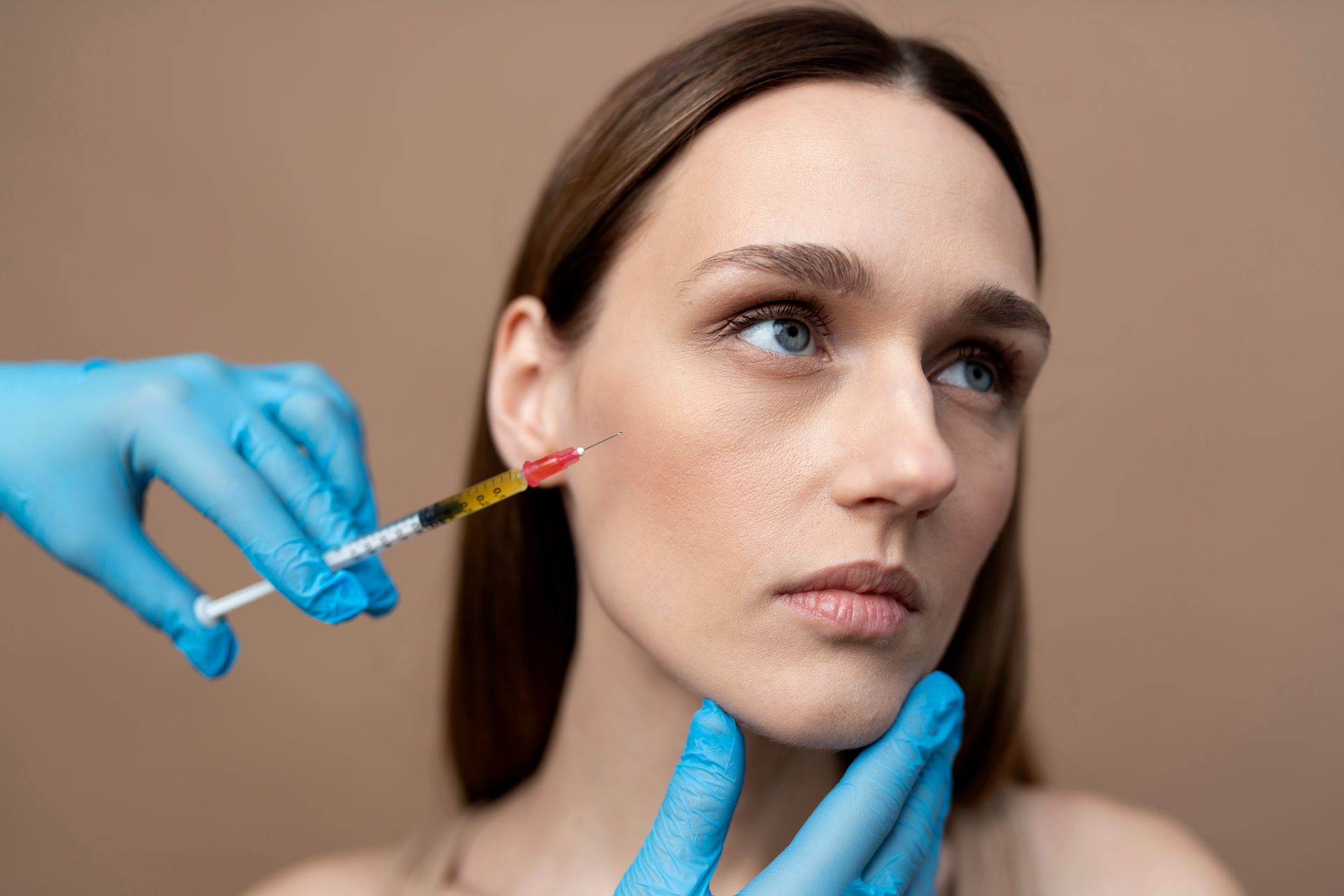 Gloved hands inject a woman’s cheek with a syringe during a cosmetic procedure
