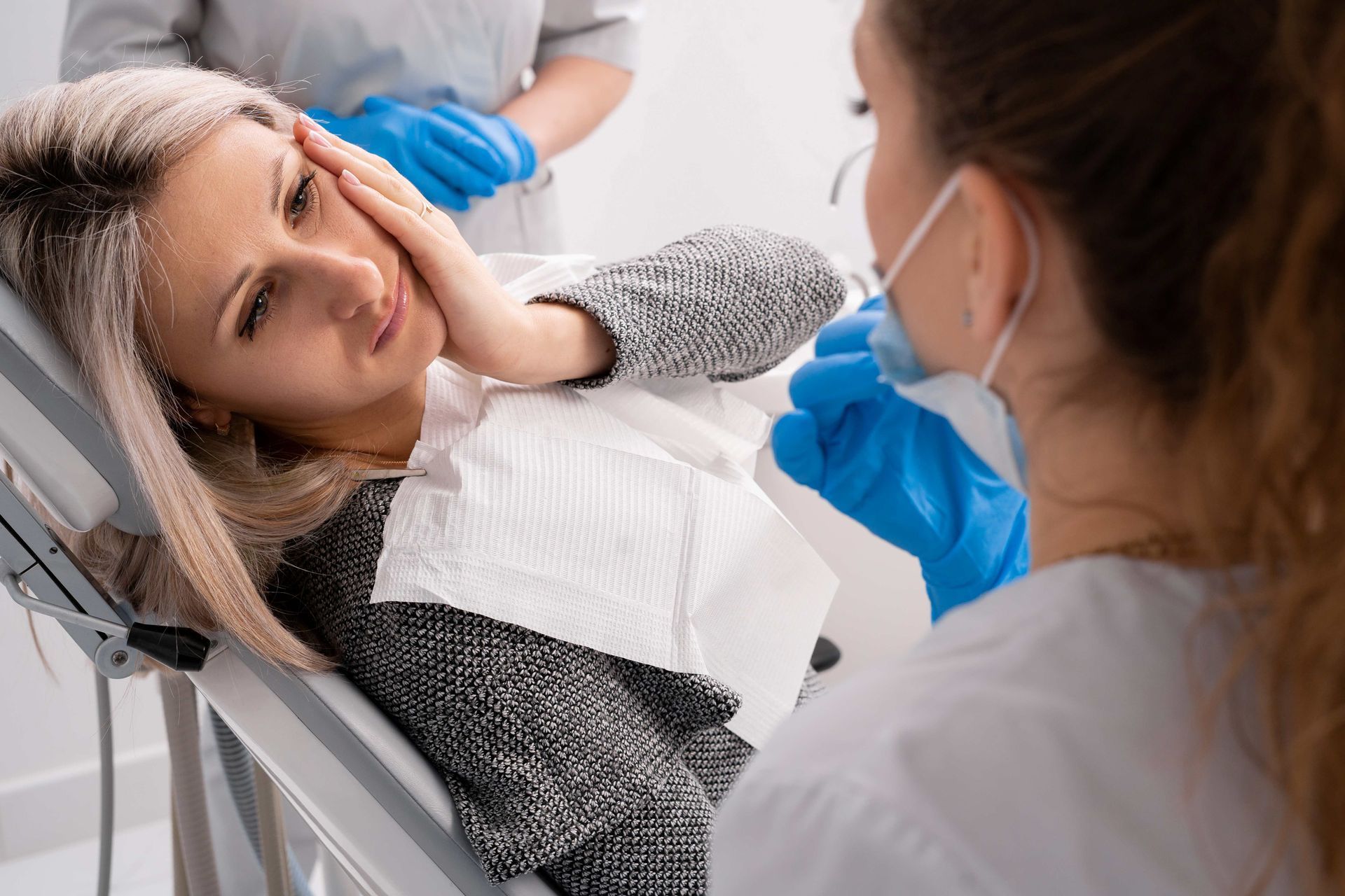 Patient holding cheek in pain during emergency dental consultation.