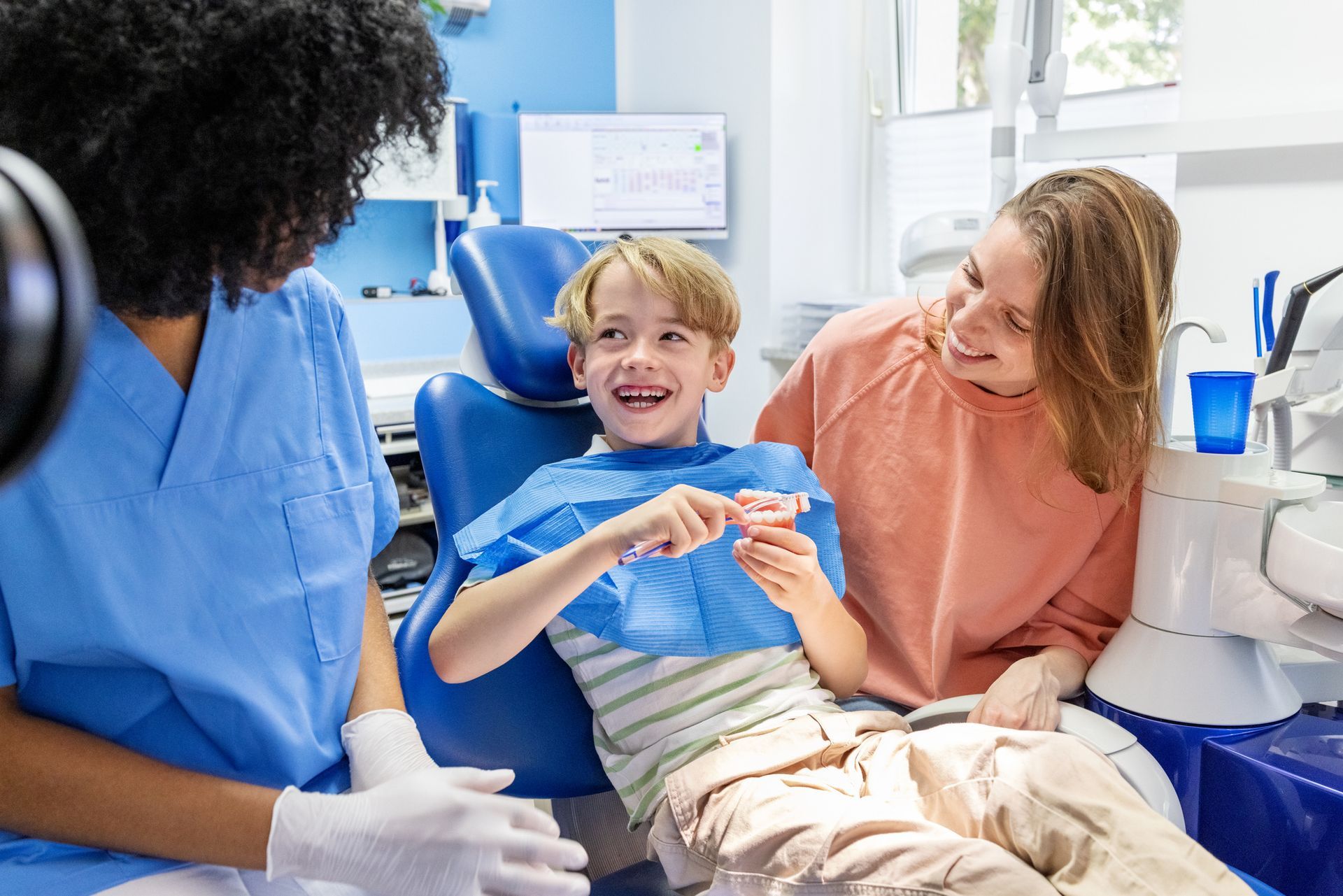 A smiling young boy sits comfortably in a dentist chair at a family dentist appointment.