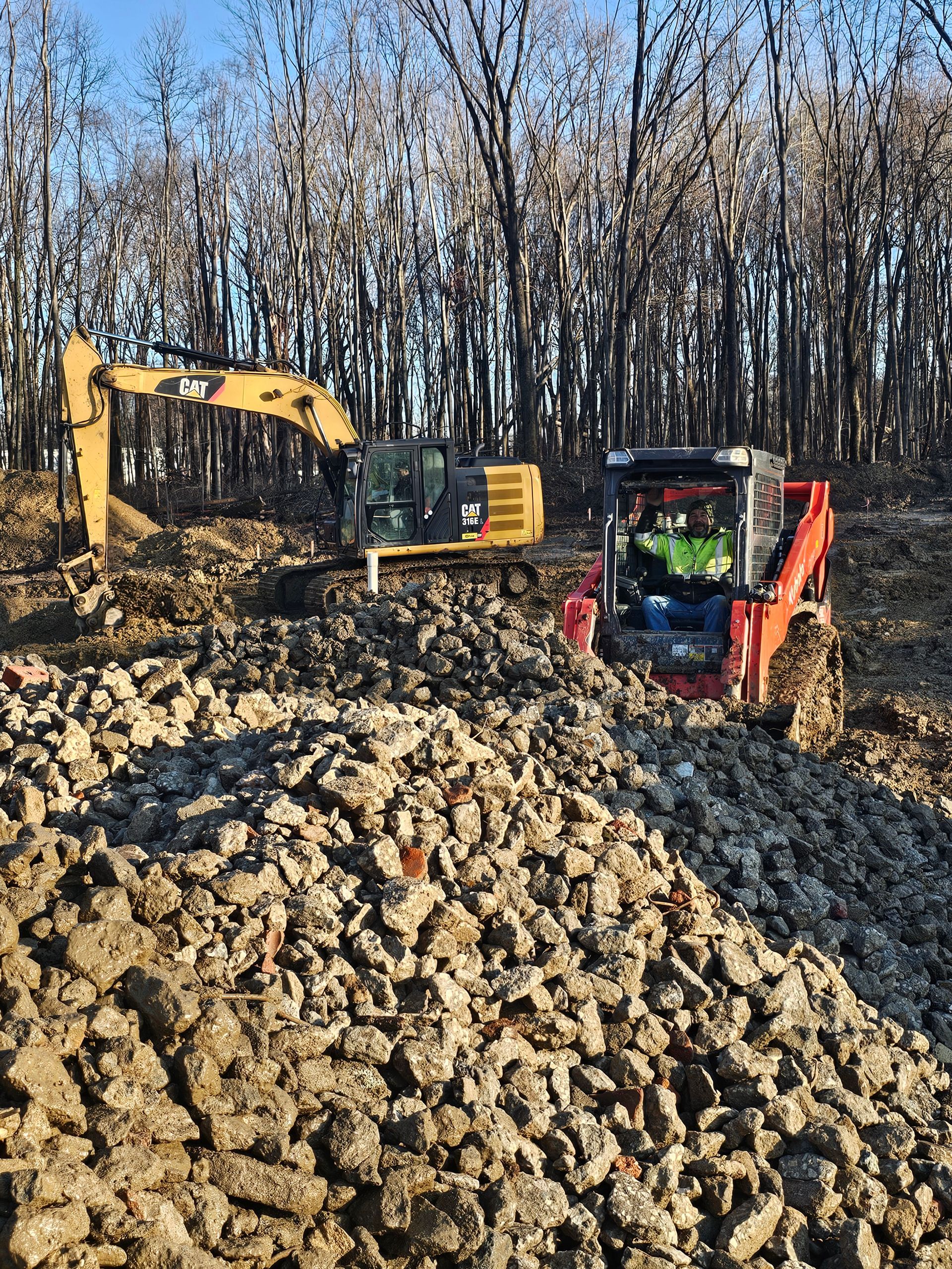 A yellow excavator and a red skid steer are working in a pile of rocks.
