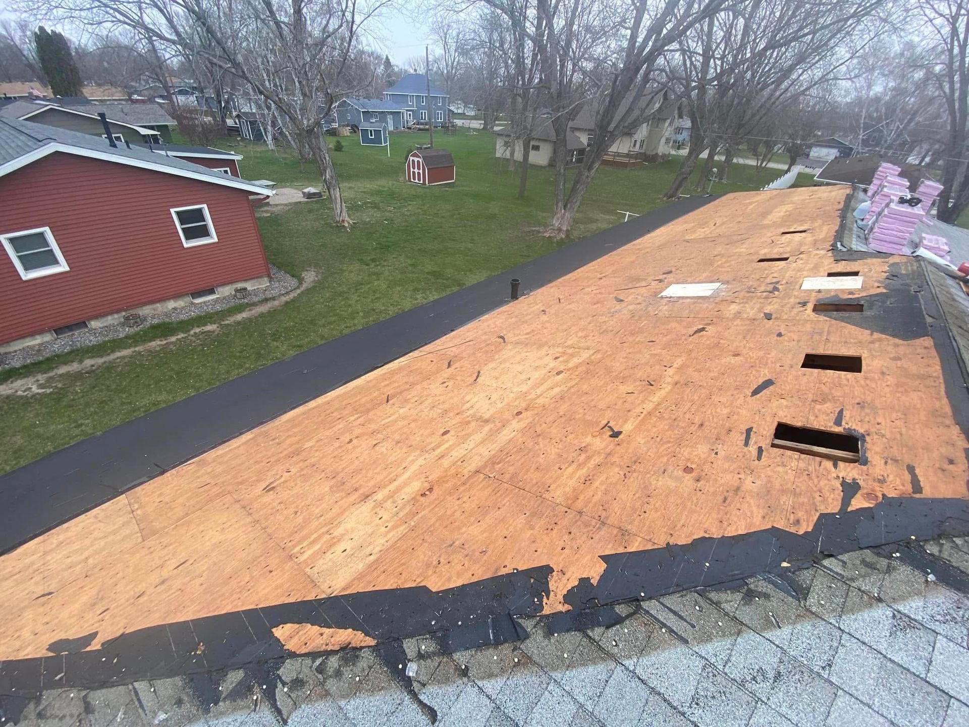 Roofover with exposed plywood and tar paper near a red shed in a suburban yard