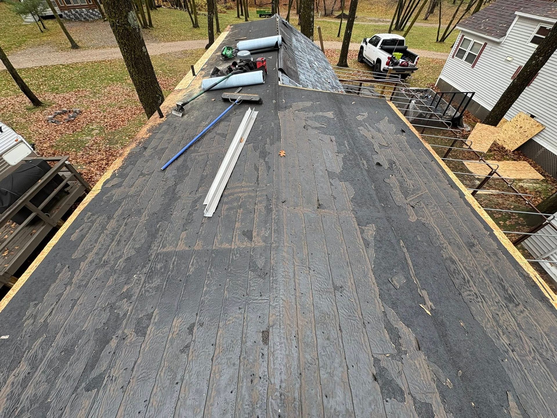 Roof under construction with black underlayment, scattered tools, and workers on a wooded property