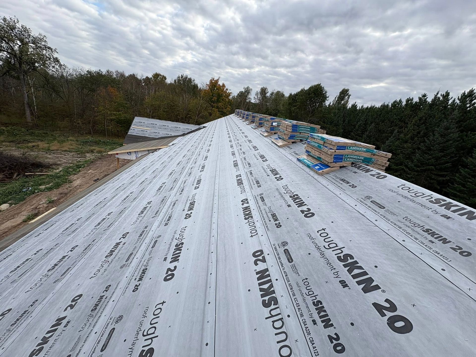 Roof underlayment on a steep roof, with trees and cloudy sky in the background