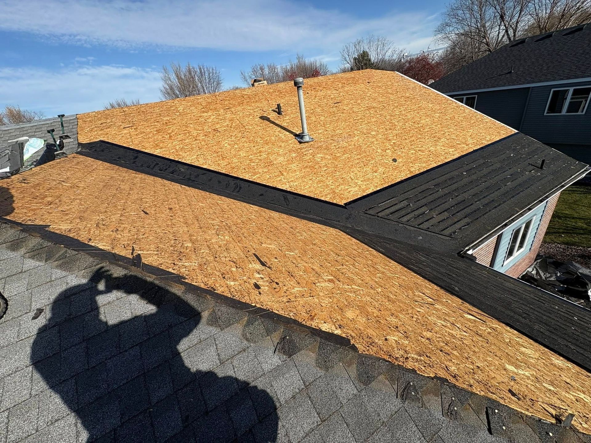 Roofer’s view of a house roof under repair, with exposed plywood and dark shingles at the edges.