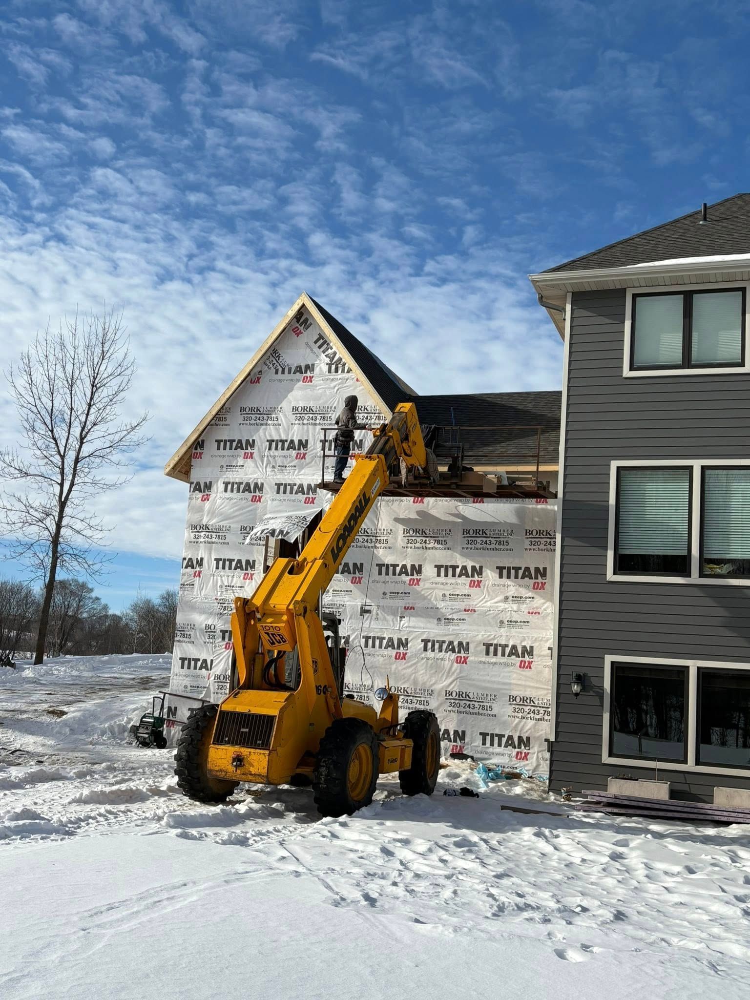 Yellow excavator working beside a house under construction in a snowy yard