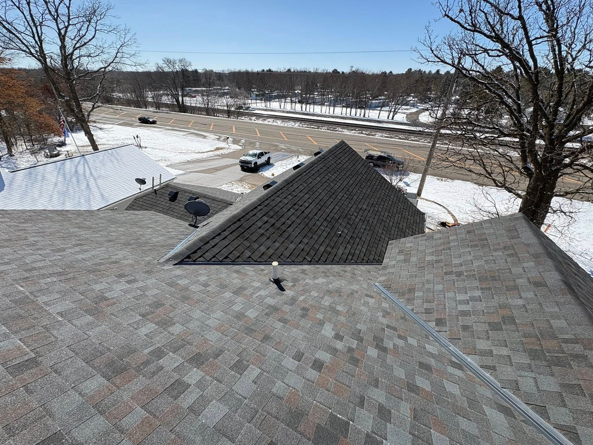 Snow-covered rooftops overlooking a frozen landscape with bare trees and a road in the distance
