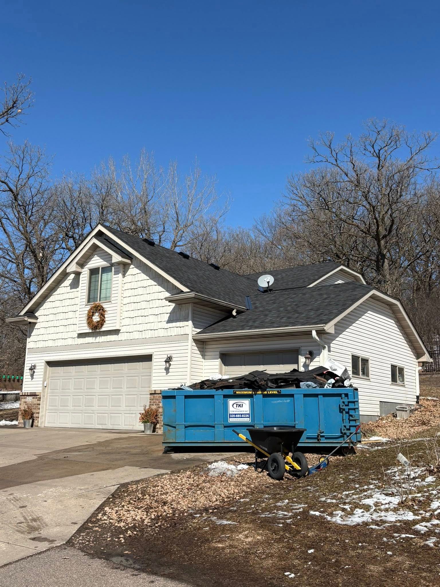 Snow-dusted suburban house with a blue dumpster in the driveway under a clear blue sky