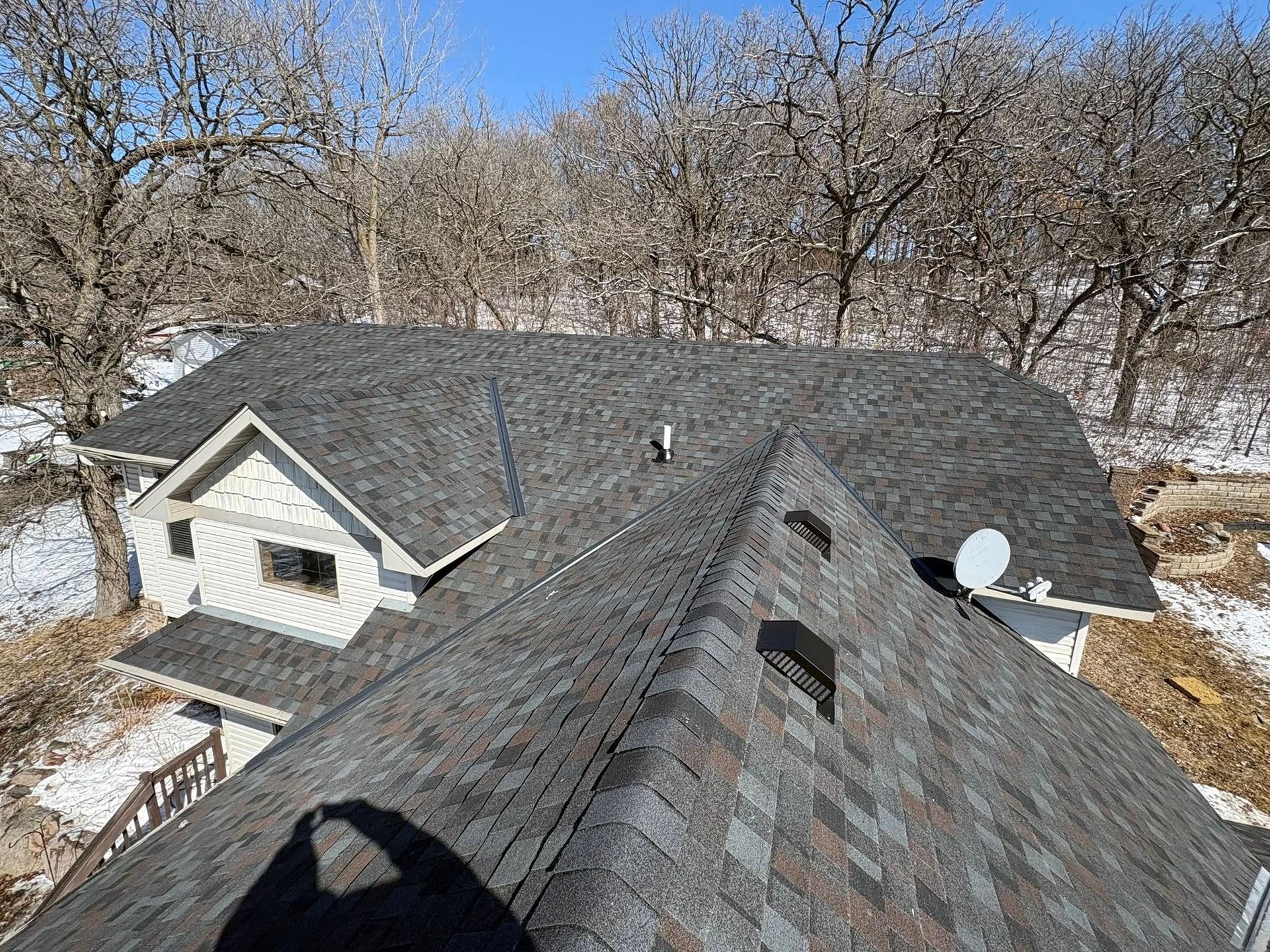 Rooftops of houses with gray shingles and bare trees in a winter yard
