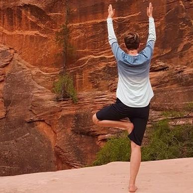 Person in tree pose, arms raised, against red rock cliff.