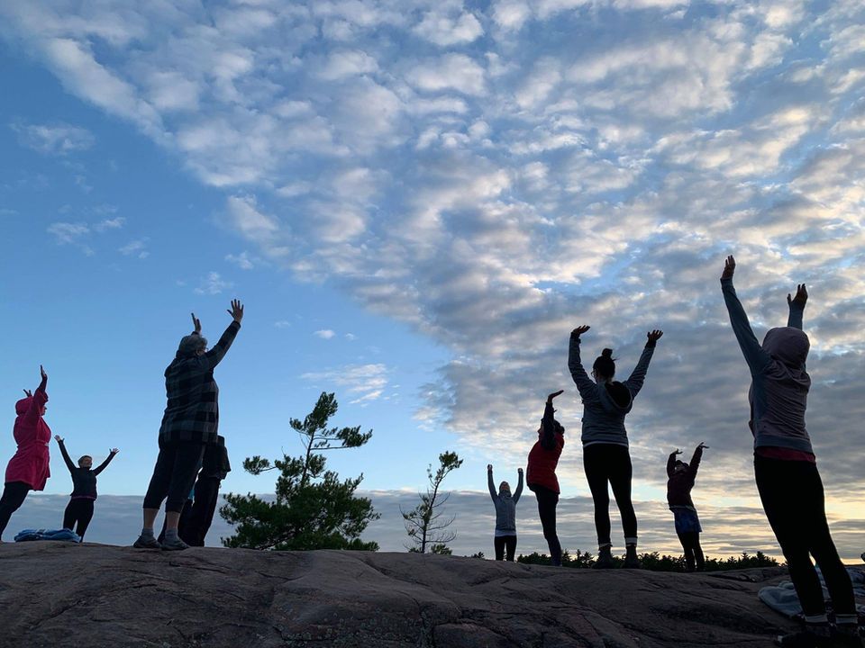 Silhouetted group on a rocky mountaintop with arms raised against a partly cloudy sky.