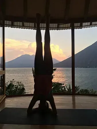 Woman in headstand pose on a mat, overlooking a lake and mountains at sunset.