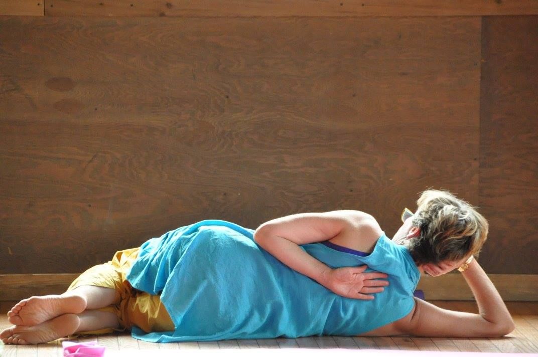 Woman in blue clothing, lying on side with arm behind back, on wood floor.