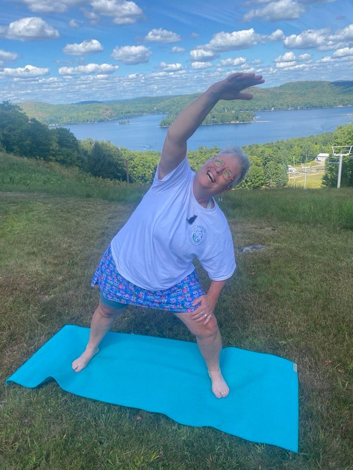 Woman stretches on a yoga mat outdoors overlooking a lake.
