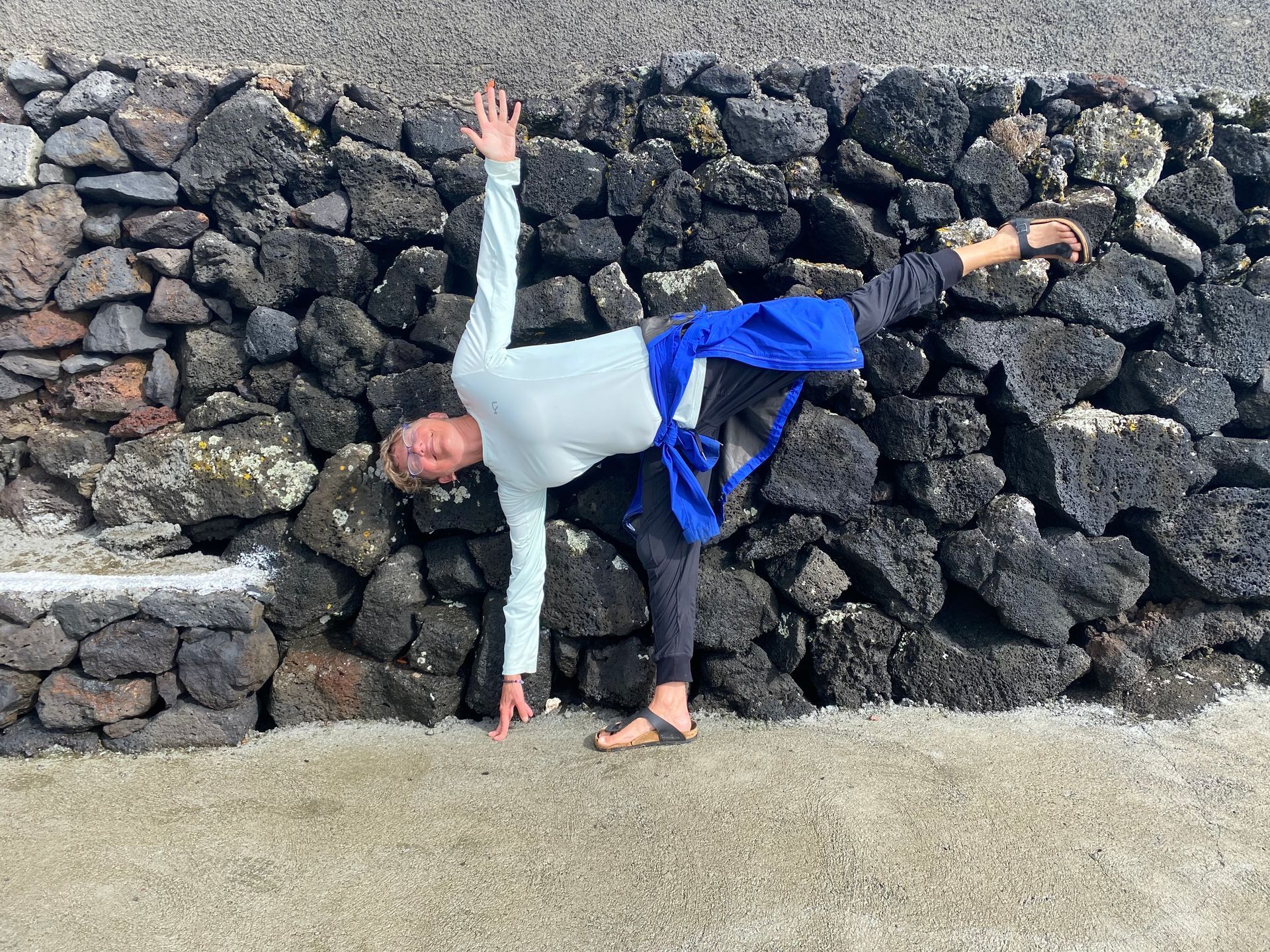 Person in a yoga pose near a dark rock wall, one leg raised, arms extended.