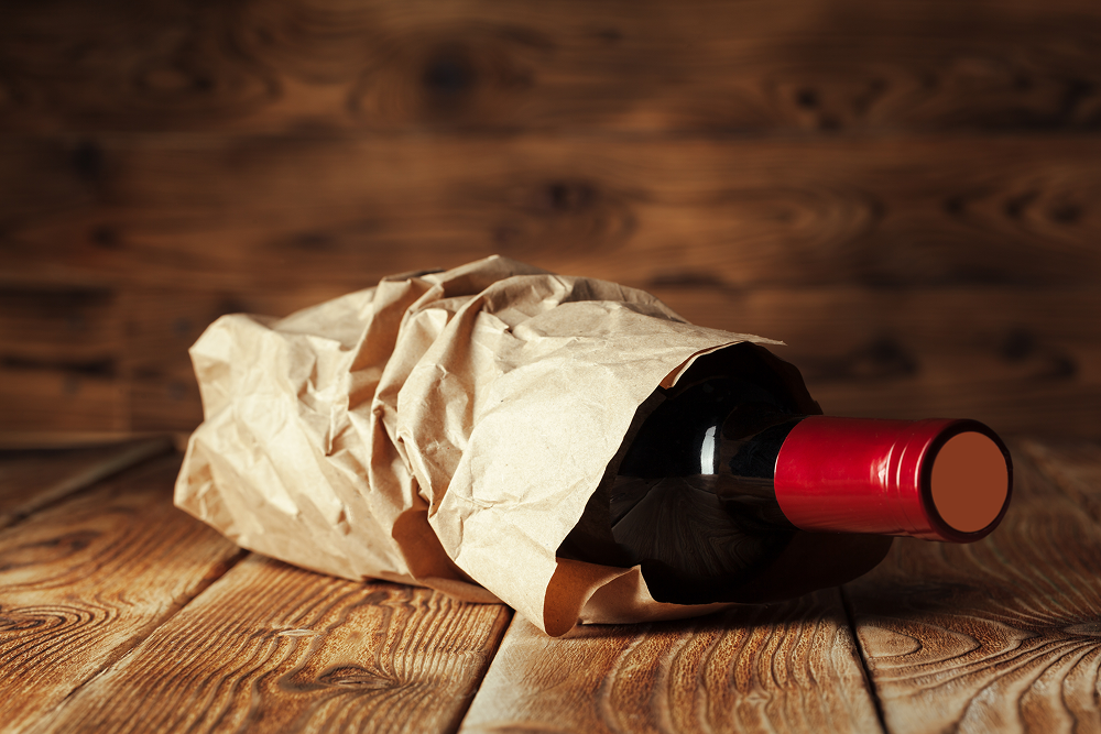 Wine bottle in a brown paper bag on a wooden surface.