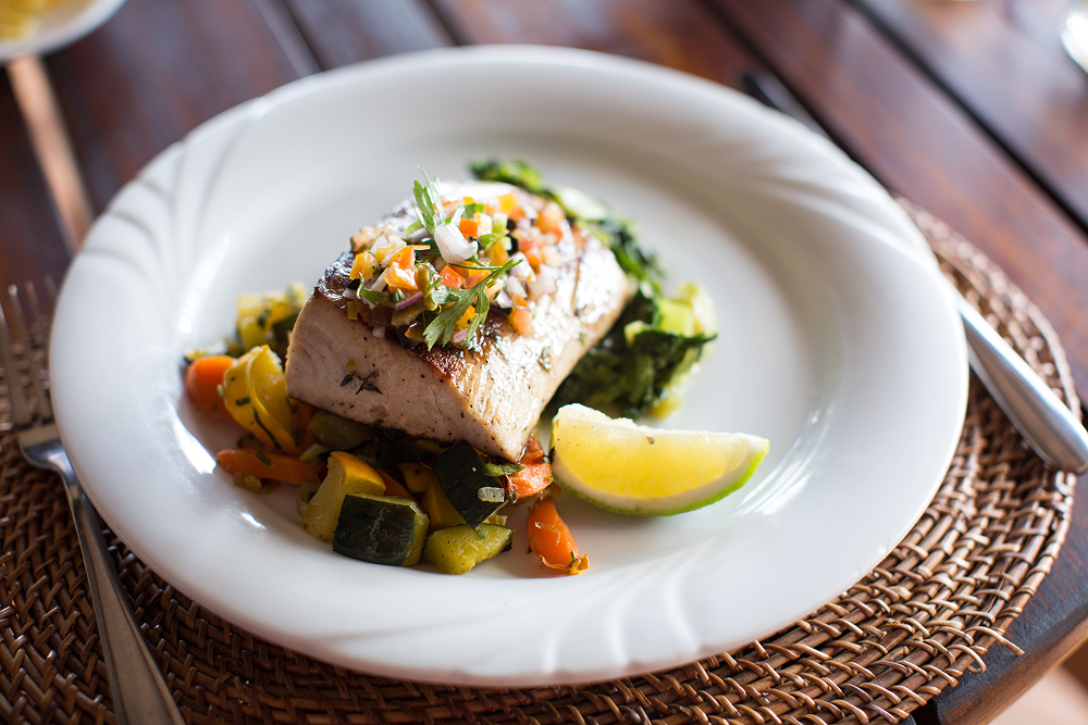 Grilled fish topped with salsa, served with vegetables and a lime wedge.