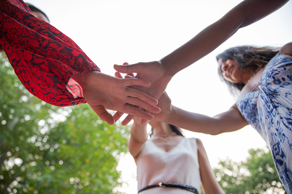 Four people with hands together, viewed from below, symbolizing teamwork.