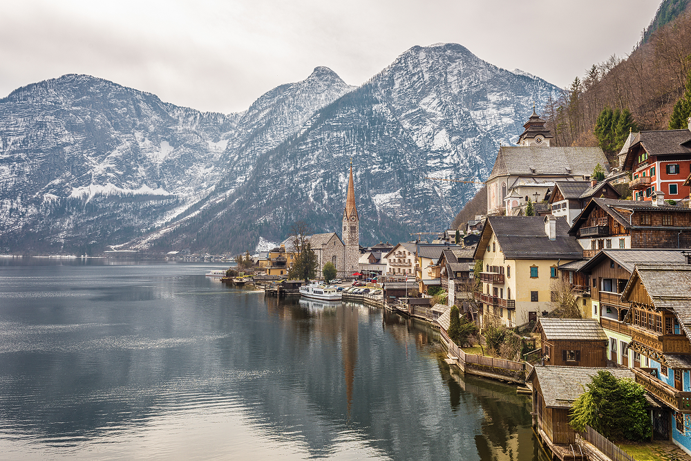 Hallstatt, Austria: Lakeside village with colorful buildings, church, and snow-capped mountains reflected in the water.