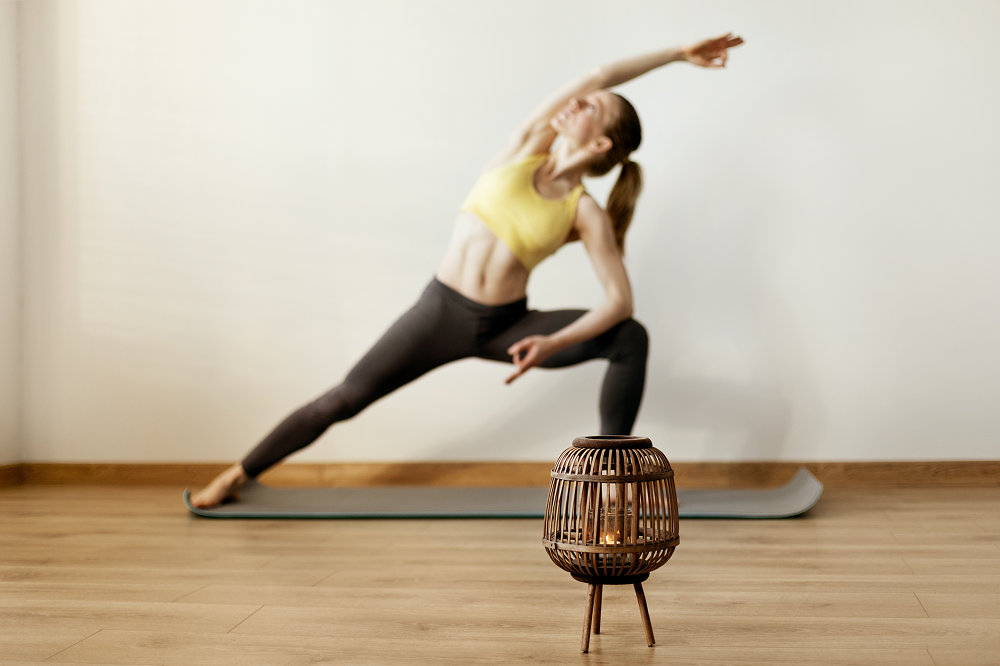 Woman in yoga pose, stretching with arm overhead, in a room with wood floor and a candle lantern.