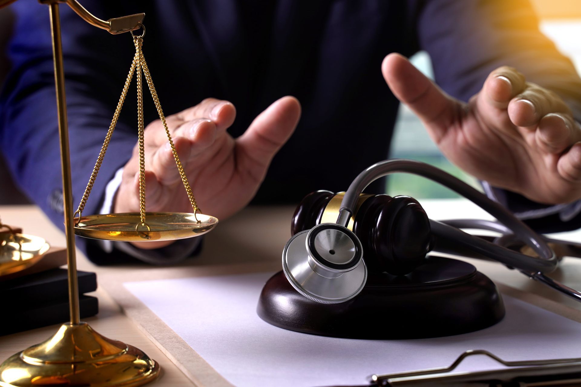 Justice scales and a stethoscope on a desk with hands gesturing nearby
