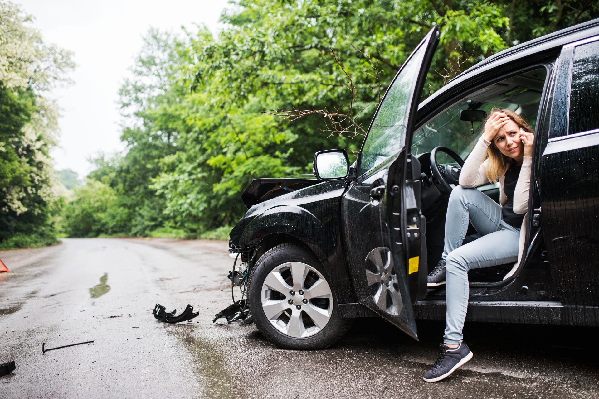 A woman is sitting in a damaged car on the side of the road.