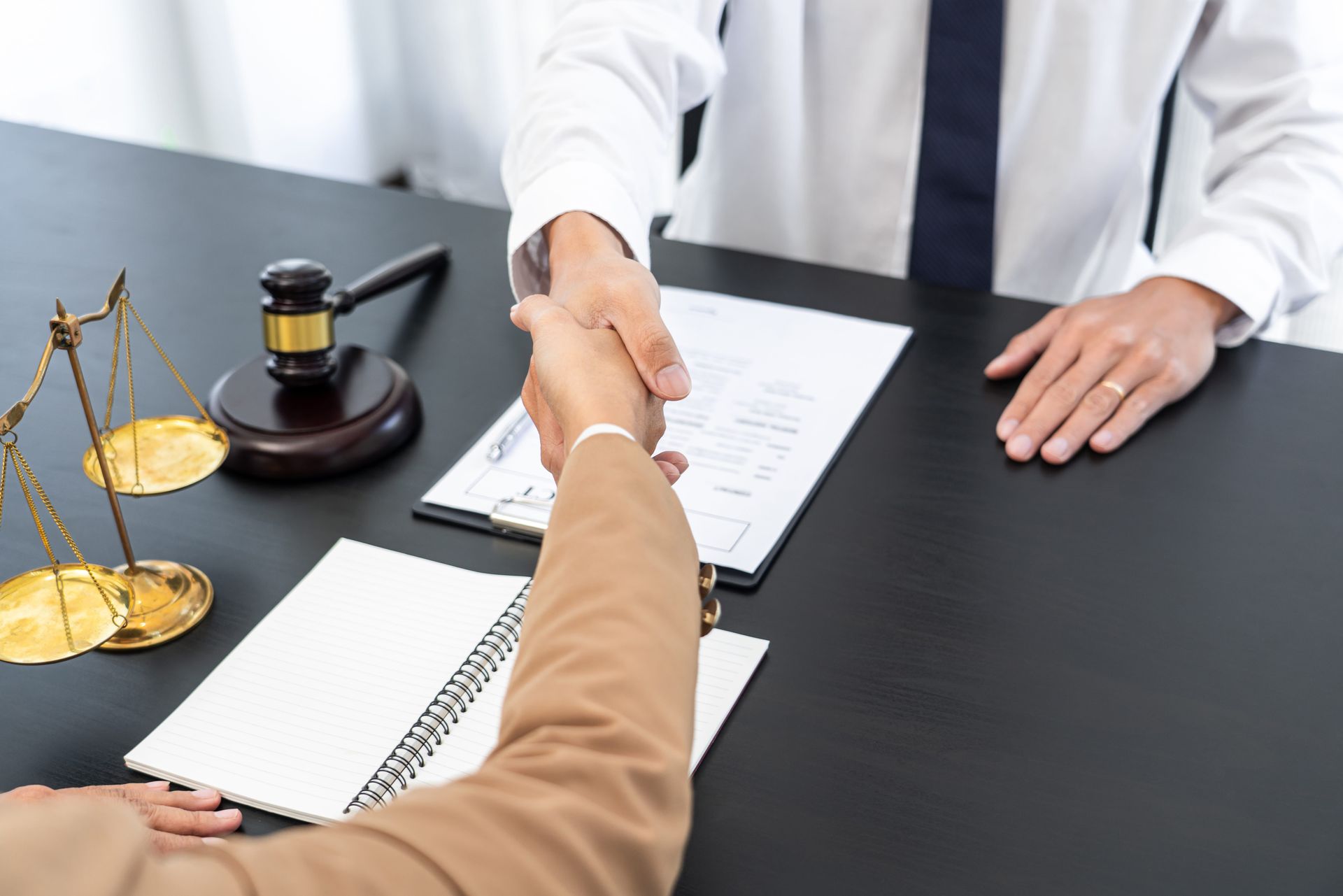 Lawyer and client shaking hands at a desk with legal documents and scales of justice