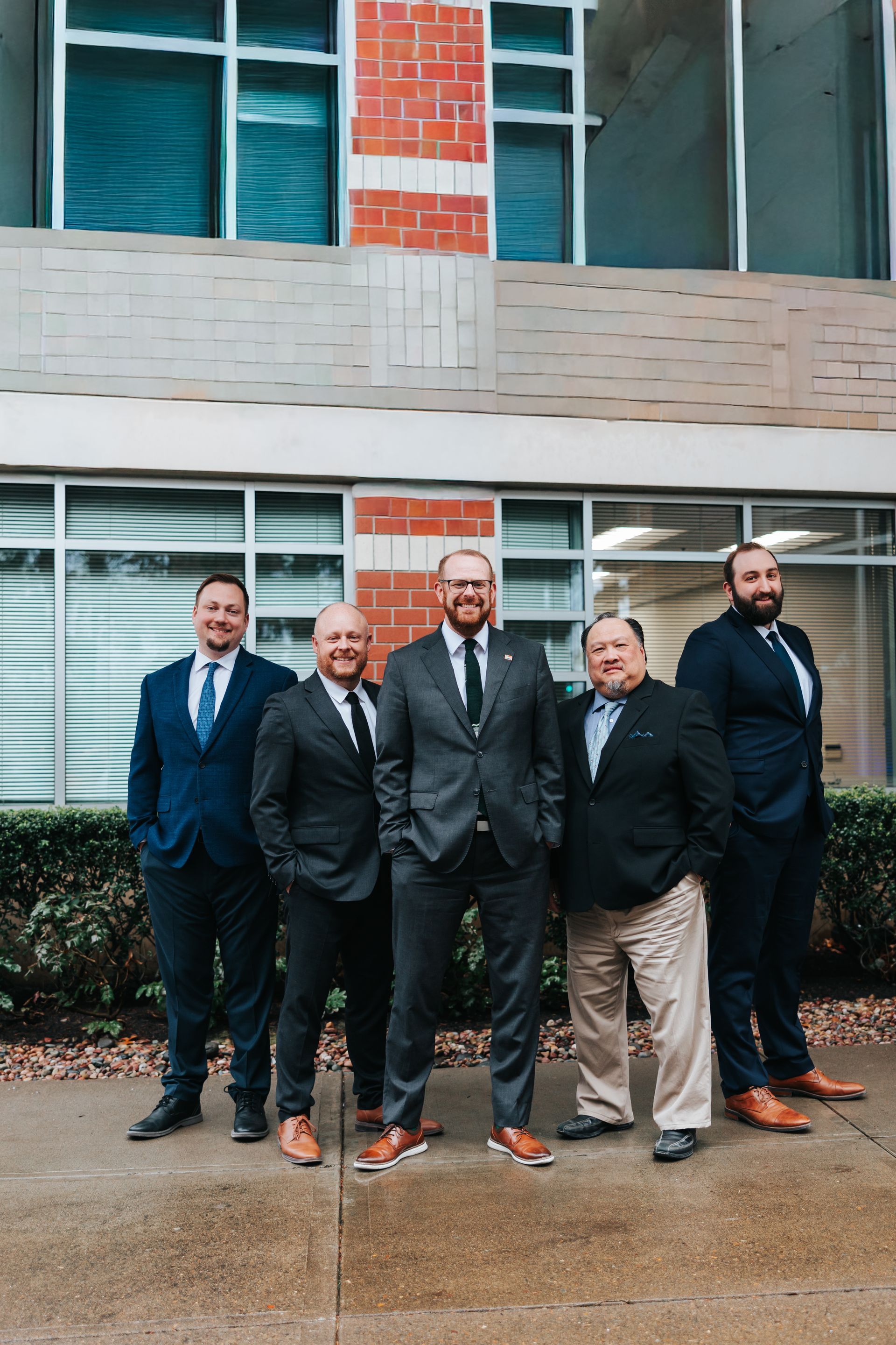 Four people in business attire pose in a brick-walled hallway.