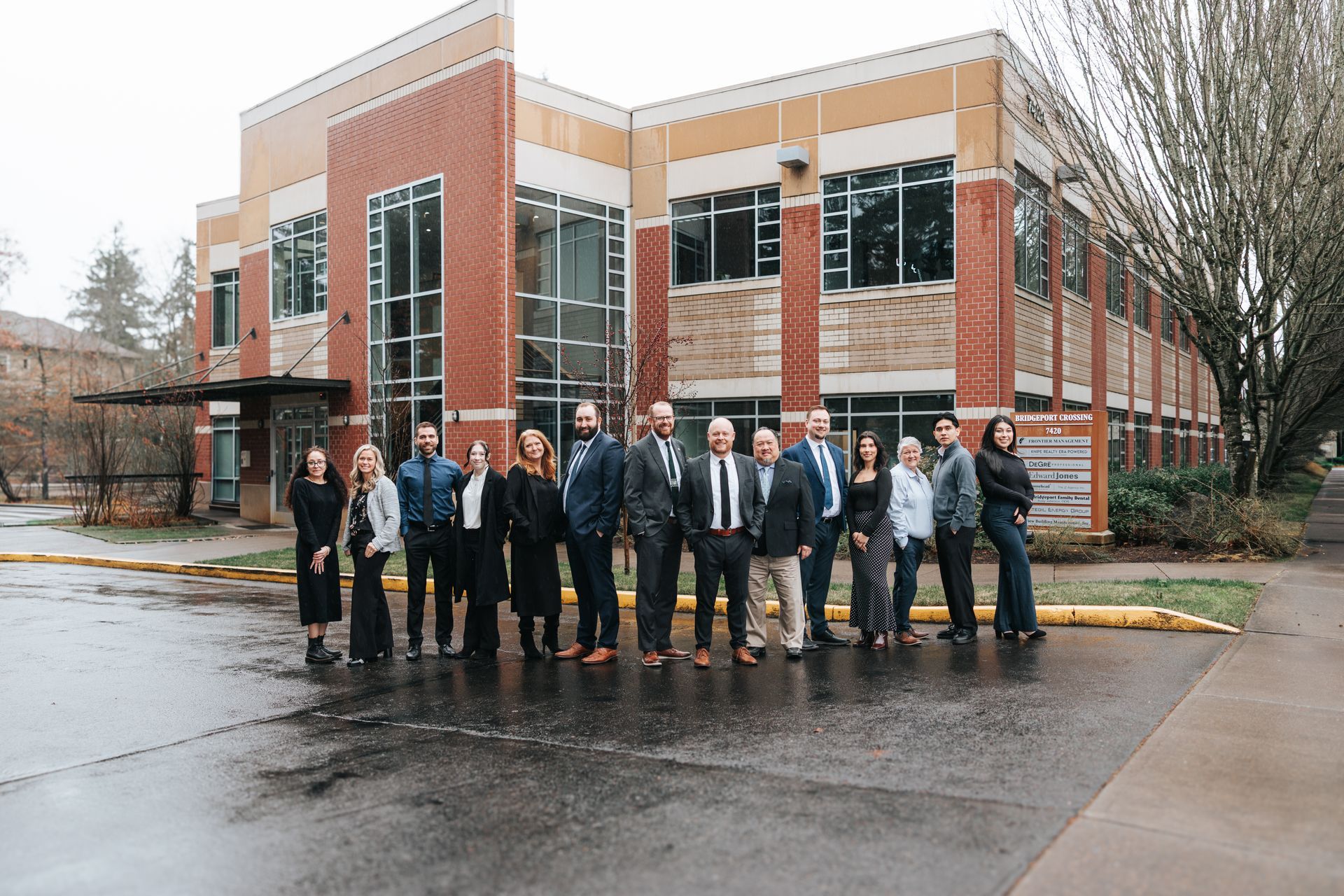 Group of people standing in front of a building with dark doors and a brick exterior.
