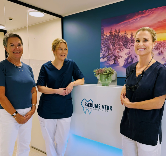 Tre personer i tannlegeklær står ved en resepsjon på et tannlegekontor.