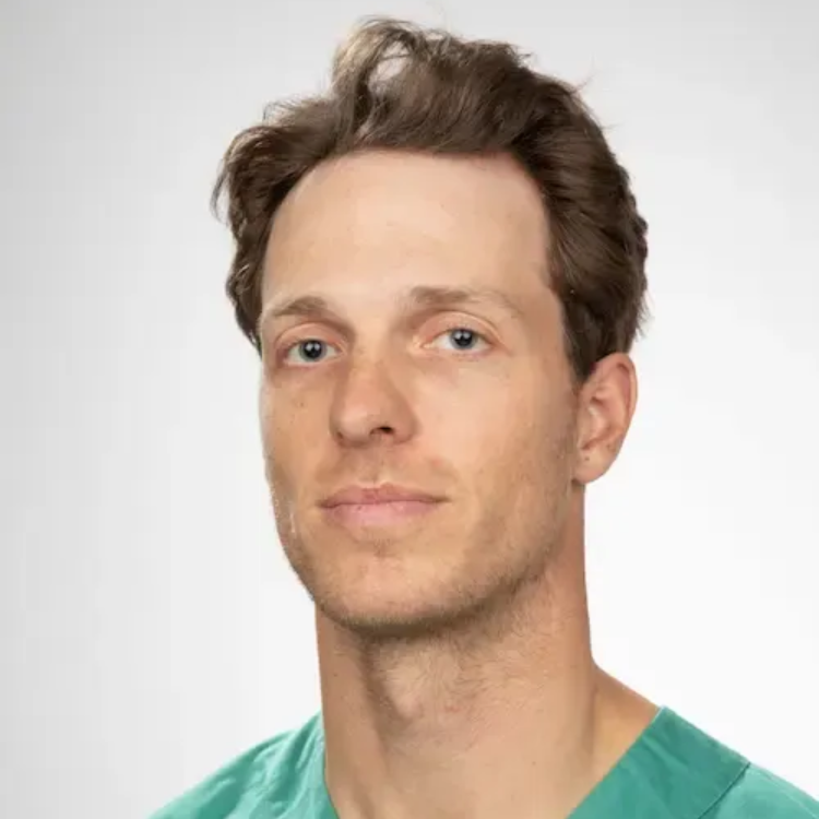 Mann med lys hud og brunt hår ser fremover, iført en grønn skrubbtopp.