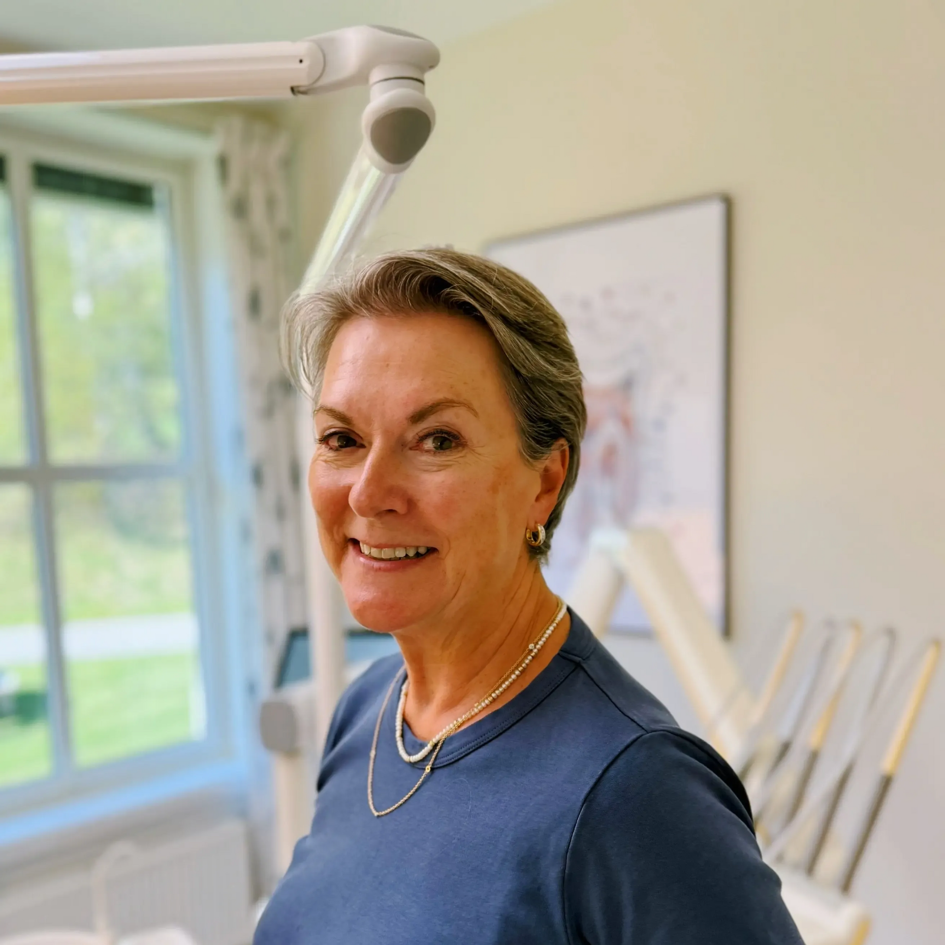 Kvinne i blå skjorte smiler på et tannlegekontor.