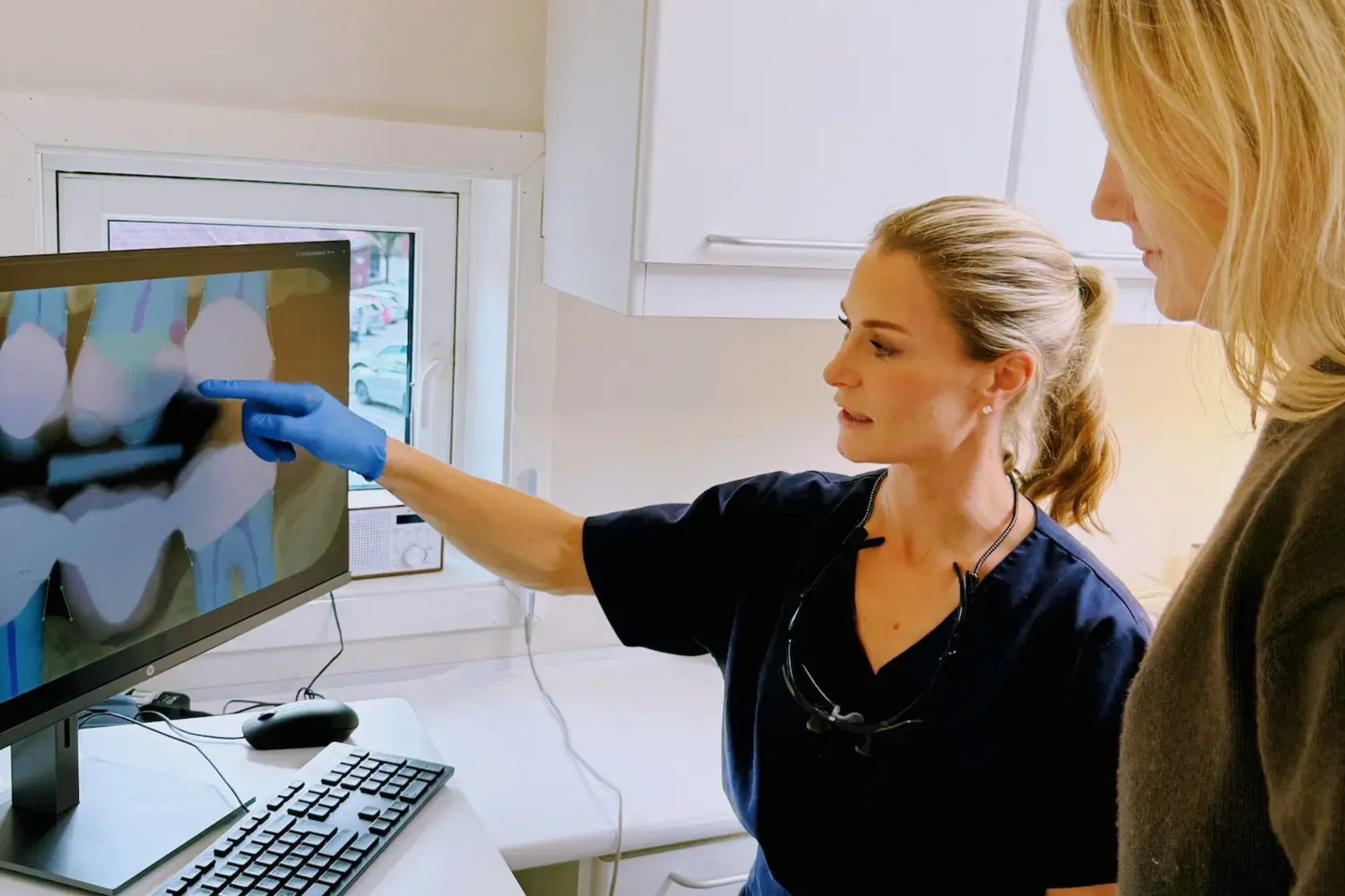 Tannlege i skrubber peker på røntgenbilde på skjermen for pasient på kontoret.