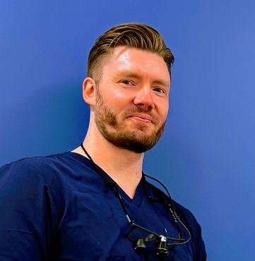 Mann med lys hud og brunt hår ser fremover, iført en grønn skrubbtopp.