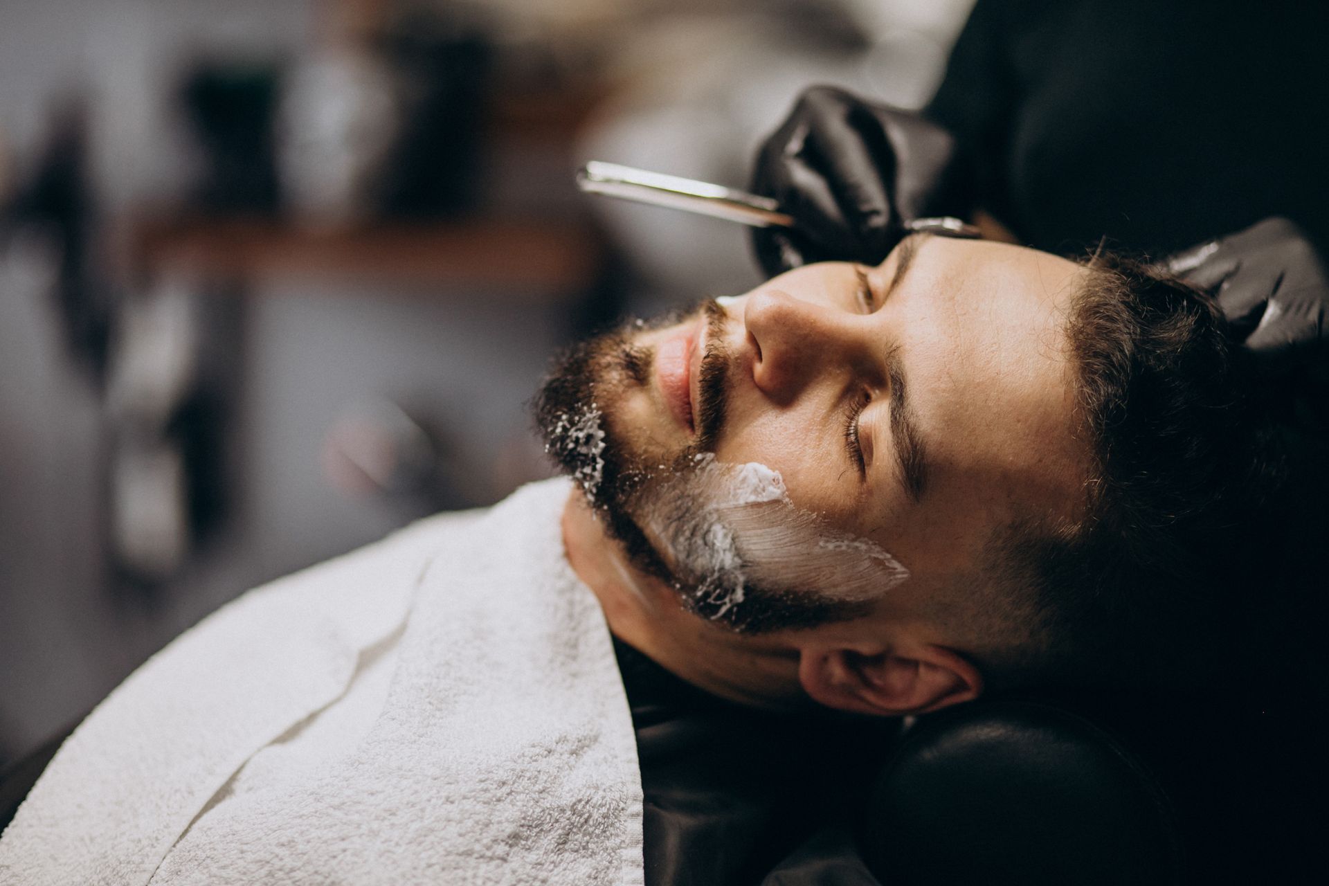 A man is getting his beard shaved by a barber in a barber shop.