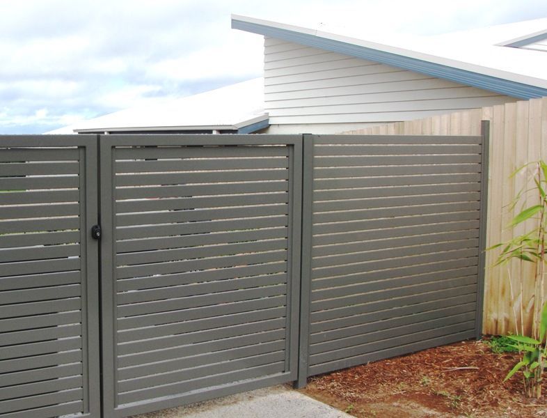 Gray horizontal slat fence with gate next to wooden fence. Cloudy sky in the background.