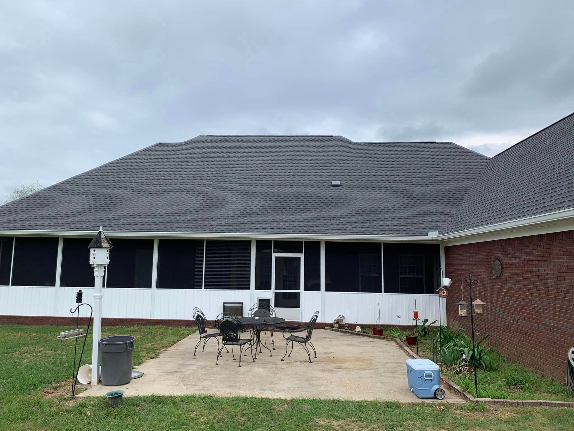 Patio with screened-in porch, dark roof, brick wall, and cloudy sky.